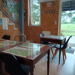 Interior de un restaurante con una mesa de madera, sillas, una escalera y vistas al exterior.