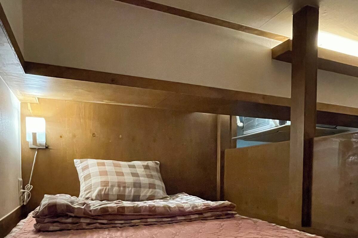 A single bed with a quilt, a wooden headboard, a bedside lamp, and a window with a view of the sky.