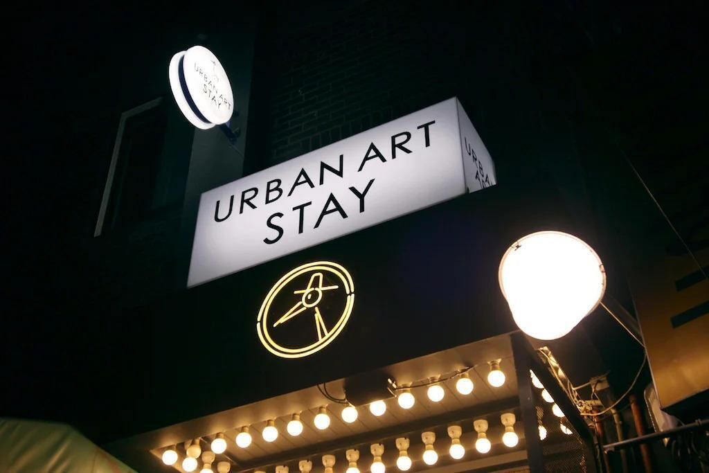 A sign for 'URBAN ART STAY' with a logo, and a row of lights below.