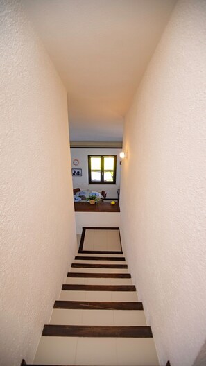 Eine schmale Treppe mit Holzdielen und weißen Wänden, die zu einem Raum mit Fenster und Tisch führt.