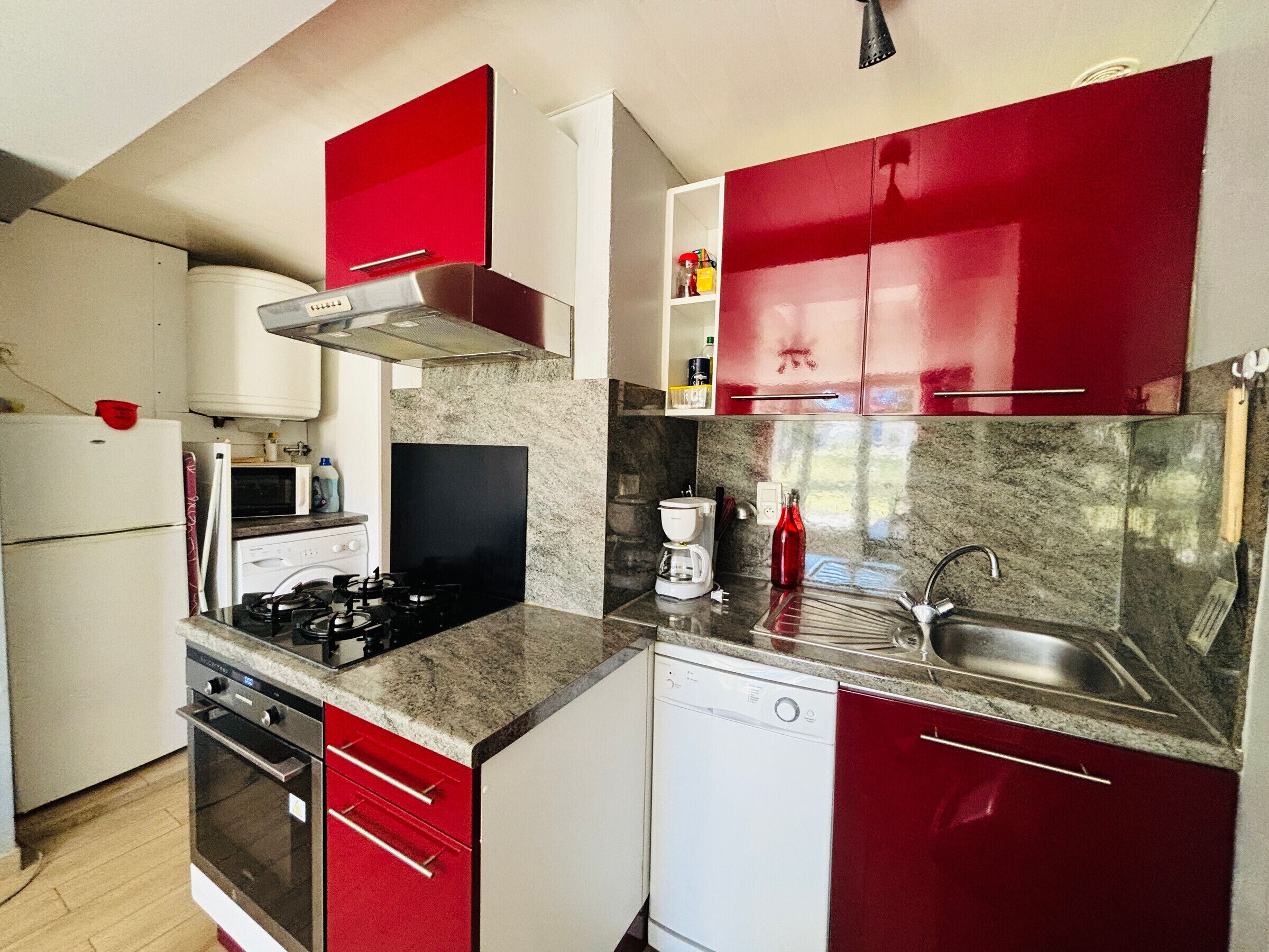 Una cocina con armarios rojos, estufa, microondas, lavavajillas y pileta.