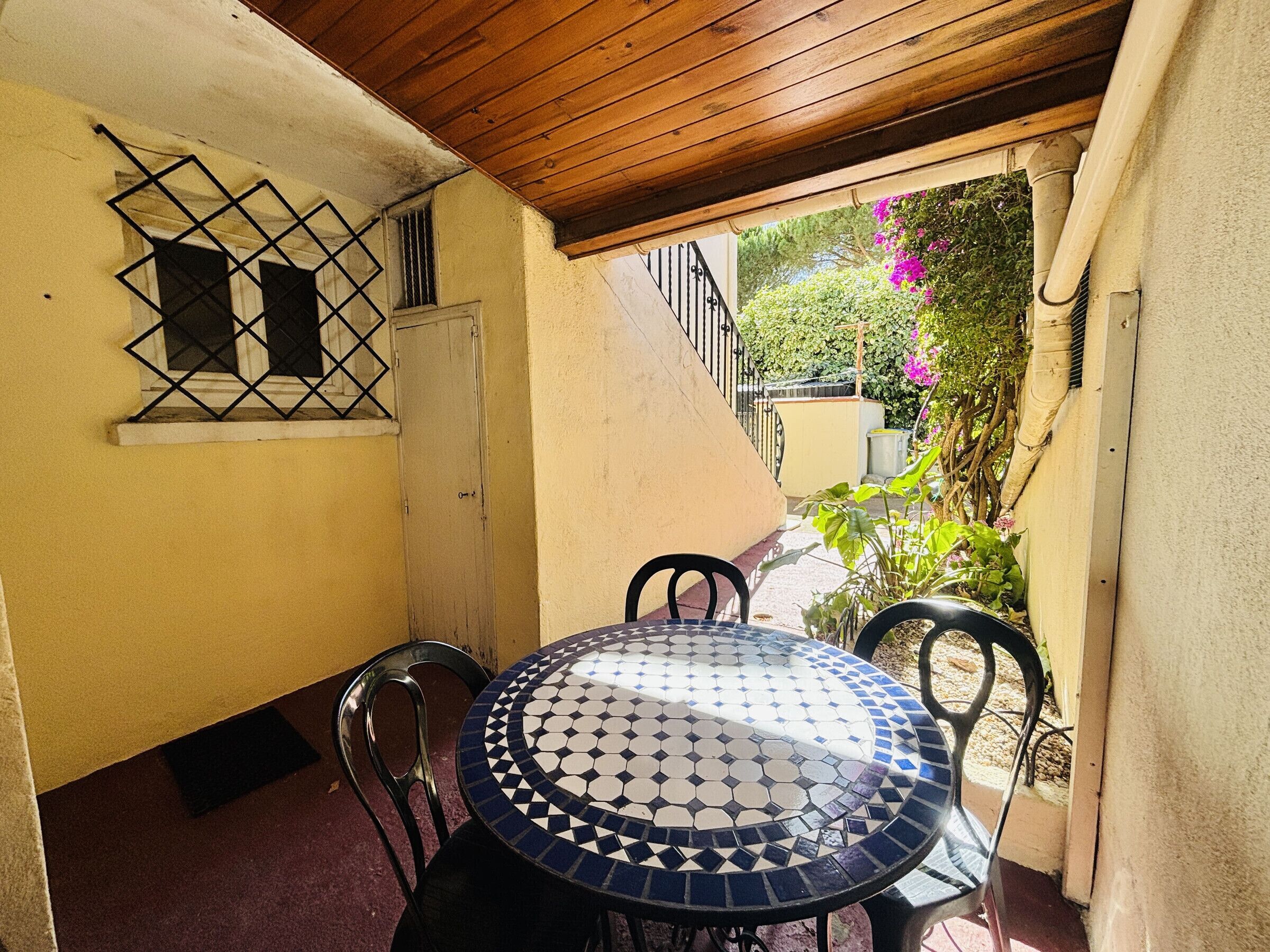 Un patio con una mesa redonda y sillas, techo de madera, una reja de seguridad fijada a la pared y una puerta.