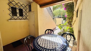 A patio with a round table and chairs, a wooden ceiling, a wall-mounted security gate, and a door.
