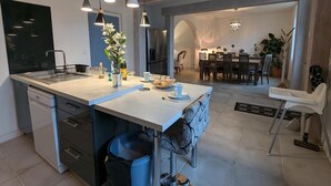 Een moderne keuken met een centraal eiland, hanglampen en een eethoek met een kroonluchter.