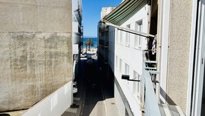 Une ruelle étroite entre deux bâtiments, d’où l’on a une vue dégagée sur une plage et des palmiers au loin.