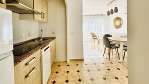 Une cuisine équipée d’une cuisinière, d’un évier et de placards, qui donne sur un coin repas avec des chaises et une table.
