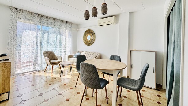 Un salon moderne avec une table à manger ronde, des chaises à revêtement gris, un canapé, un miroir décoratif et des rideaux à motifs.