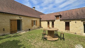 A courtyard with a round wooden table and stools, stone buildings with tiled roofs, and a clear sky. - House in Périgord, parking, pets allowed - 4 guests (Campagne)