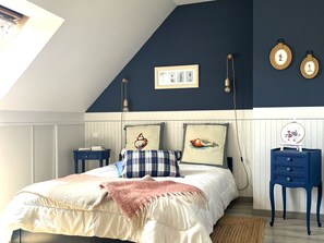 Ein Schlafzimmer mit schrägem Dach, einem Bett mit vielen Kissen, zwei Nachttischen und Wandleuchten.