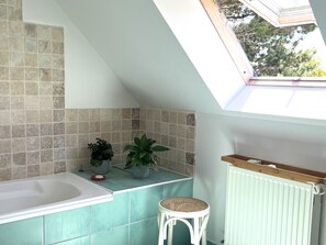 Ein Badezimmer mit Oberlicht, Badewanne, einer kleinen Bank und Topfpflanzen.