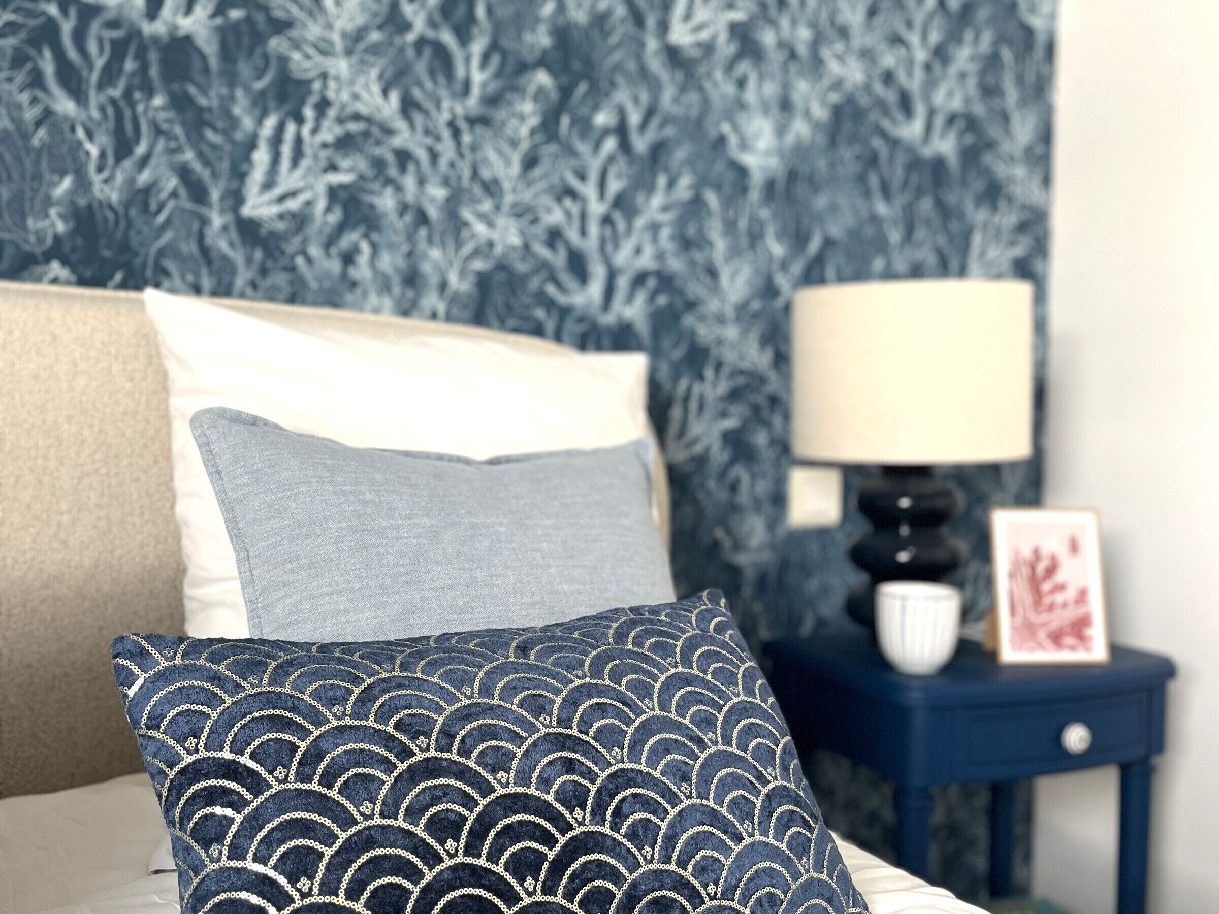 Een bed met kussens, een nachtkastje met een lamp en een muur met behang.