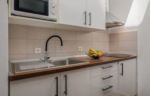 Uma cozinha moderna com uma pia de aço inoxidável, micro-ondas e uma fruteira no balcão.