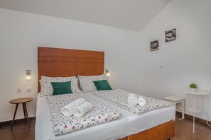 Una cama doble con ropa de cama floral, un cabecero de madera, dos almohadas verdes y una mesita de noche con una lámpara.