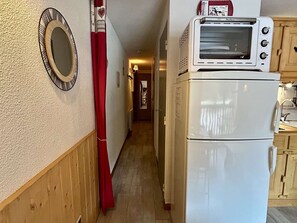 Un pasillo estrecho con un refrigerador blanco, un microondas encima y una cortina roja.