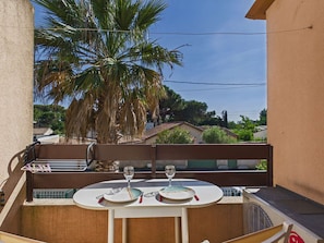 Ein Balkon mit Tisch für zwei Personen, einer Palme und Blick auf Häuser.