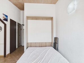 Een slaapkamer met een bed, een houten hoofdbord, een witte muur en een deur.