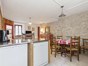 A compact kitchen with a dishwasher, a dining area with a table set for two, and a stone wall. - Charming house, pets welcome - 5 guests (Arreau)