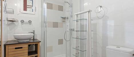 Un baño con cabina de ducha de vidrio, un lavamanos blanco y un inodoro.