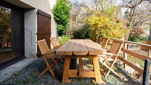 Een houten tafel met stoelen buiten een gebouw, op een grindpad.