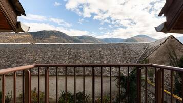 A rustic building with a sloped roof, a metal railing in the foreground, and a mountainous landscape in the background.