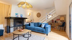 Een moderne woonkamer met een open haard, een blauwe bank, een ronde salontafel en een trap naar een hoger gelegen verdieping.