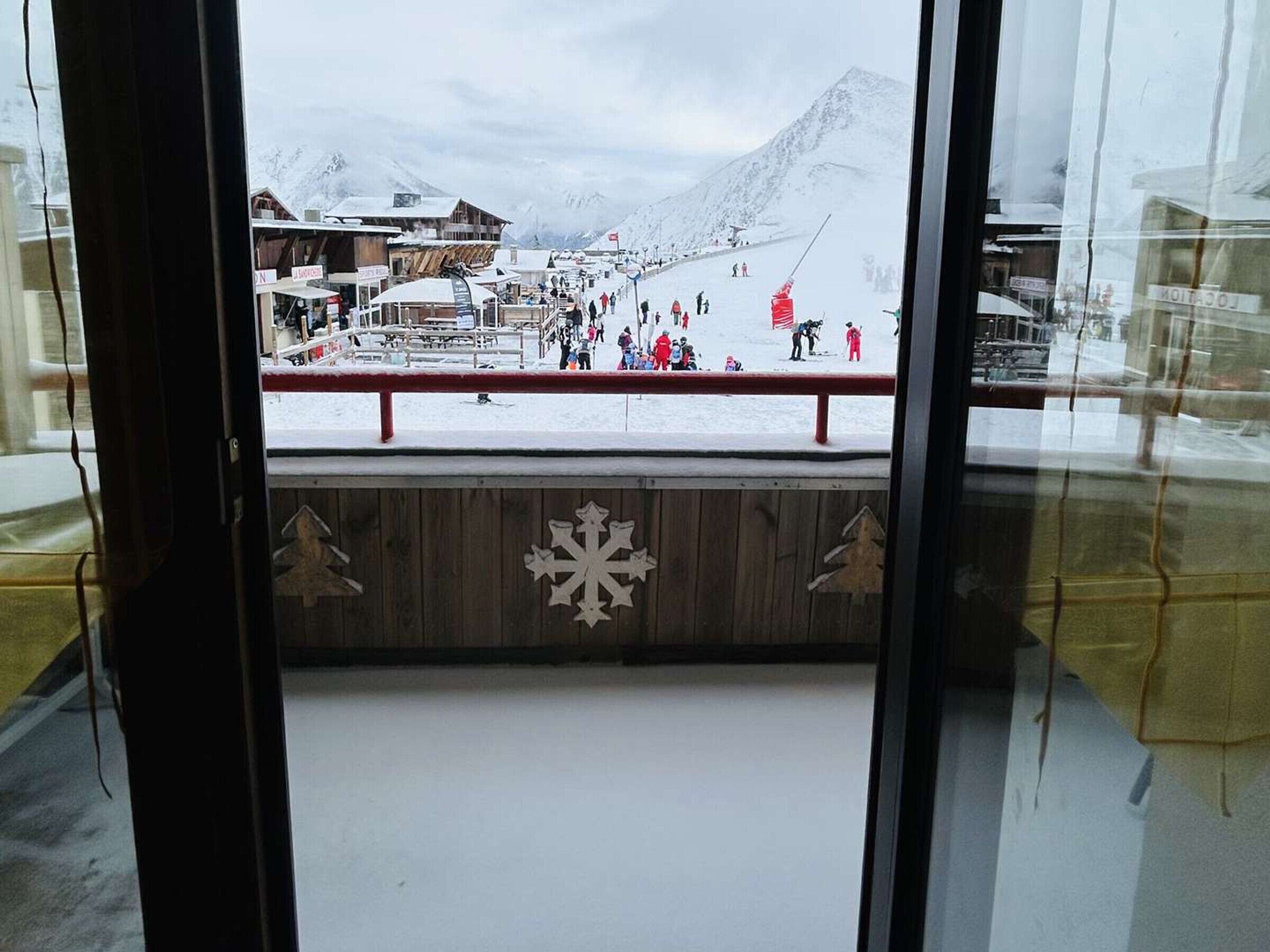 A view of a snowy mountain area with a ski slope, buildings, and a wooden structure with snowflake decorations.