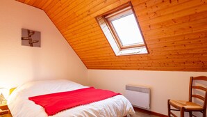 A bedroom with a sloped wooden ceiling, a skylight, a bed with white bedding and a red blanket, a wooden chair, and a radiator.