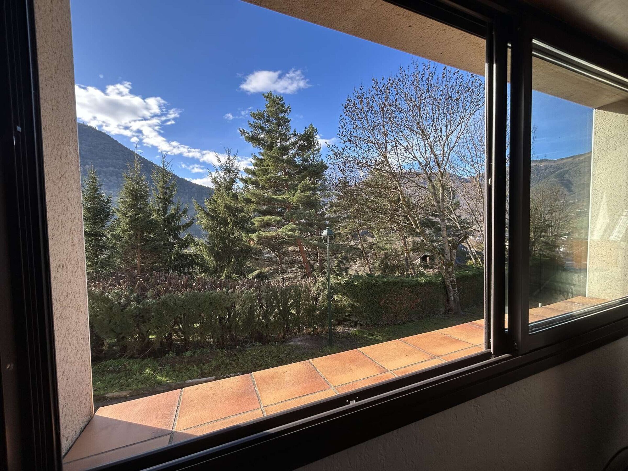 Ein Fenster mit Blick auf eine Berglandschaft, Bäume und einen klaren Himmel.