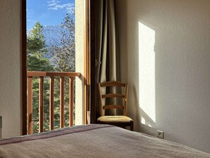 A room with a bed, a wooden chair, a balcony with a view of mountains, and a window with curtains. - Spacious house, garden, mountain view - 10 guests (Arreau)