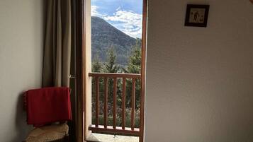 A room with a wooden chair, a red towel, a balcony with a wooden railing, and a mountain view.