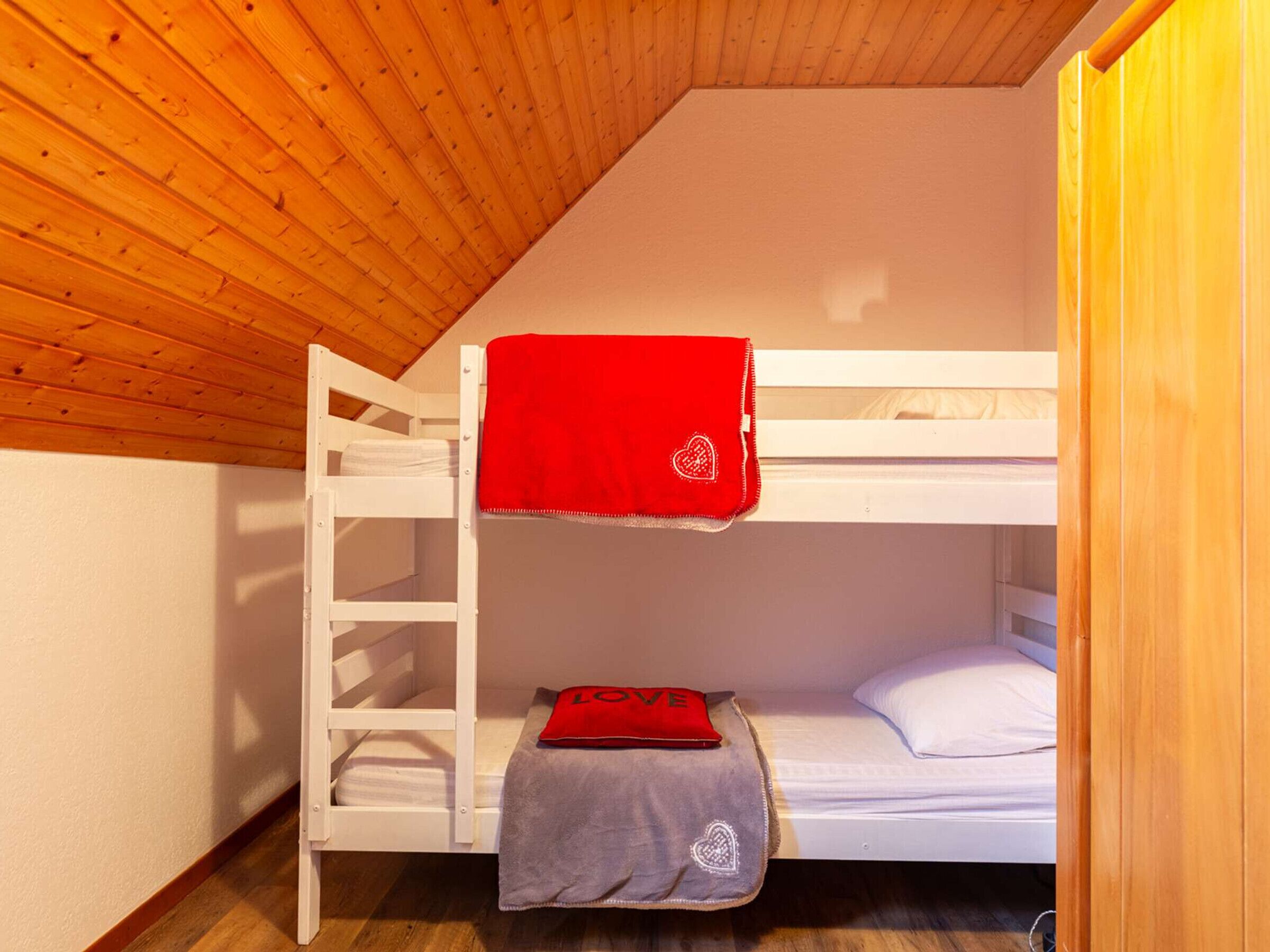 Une chambre avec des lits superposés, un plafond en bois et des murs blancs.