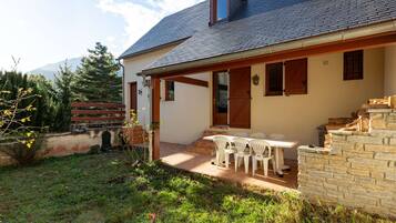 A house with a stone staircase, a covered patio with outdoor furniture, and a mountain in the background.