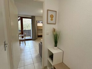 A hallway with a door leading to a balcony, a framed picture on the wall, and a small white shelf with a plant. - Studio cabin with wifi and parking - 4 guests (Arreau)