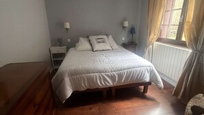 A bedroom with a bed, two bedside tables, a window with curtains, and a radiator. - Single-storey house with garden - 6 guests (Cadéac)