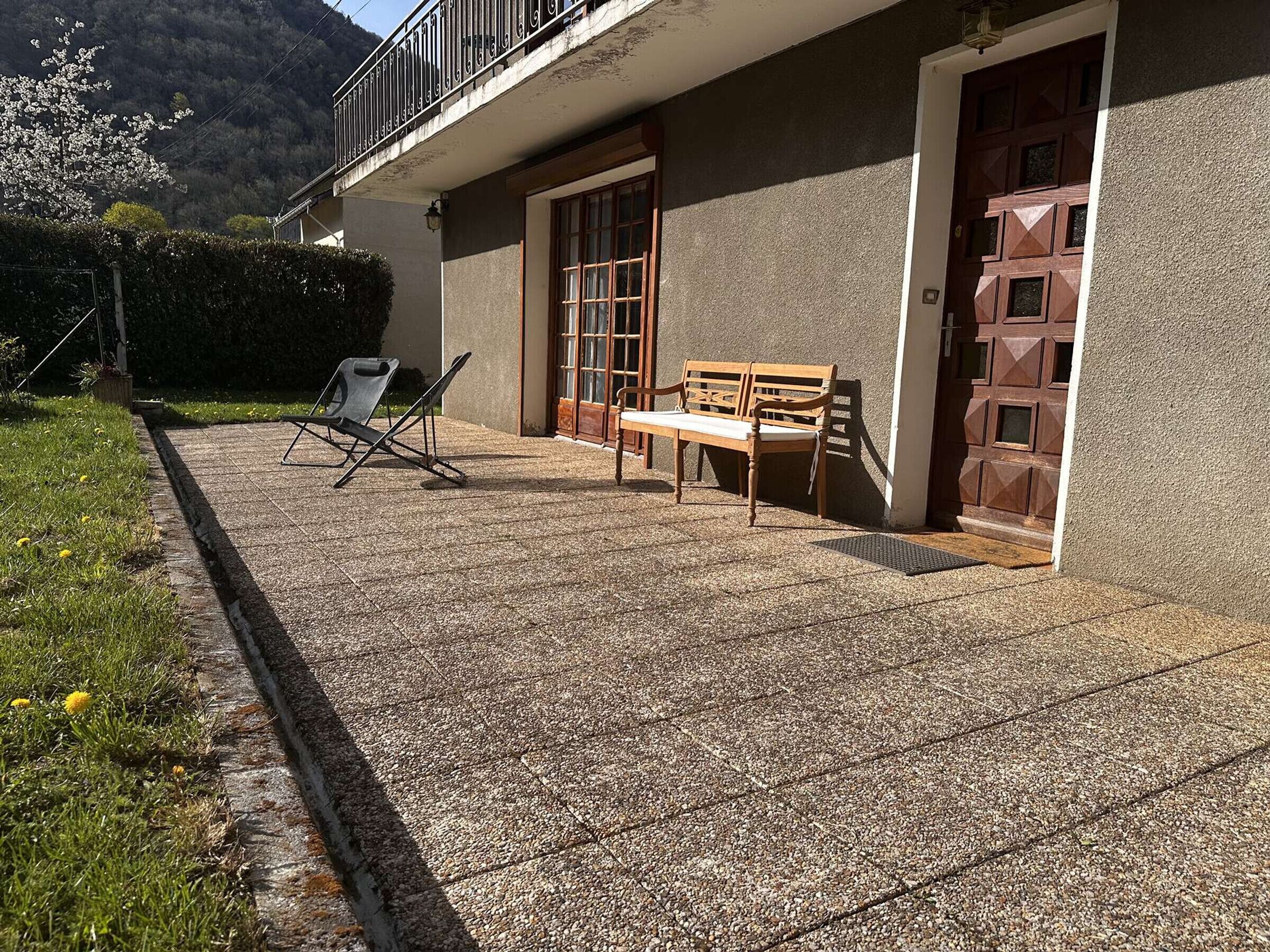 A building with a balcony, a wooden bench, and a folding chair on a paved patio.