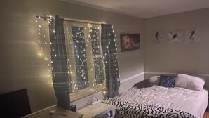 Quarto com cama, escrivaninha, janela decorada com luzes e pintura na parede.
