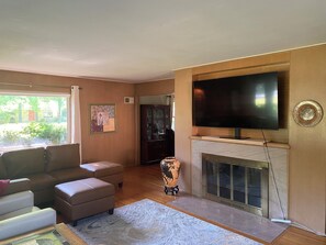 Un salon avec un canapé, un pouf, une cheminée, un téléviseur et un tableau accroché au mur.