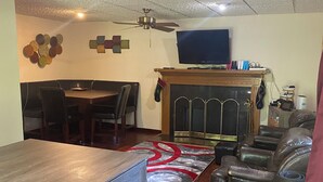 Uma sala de estar com uma mesa de jantar de madeira, lareira, assentos de couro e um ventilador de teto.