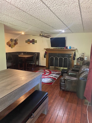 A living room with a wooden dining table, a fireplace, leather seating, and a ceiling fan.