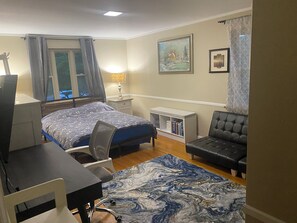 Um quarto com cama, escrivaninha, cadeira, sofá, estante de livros e janela com cortinas.