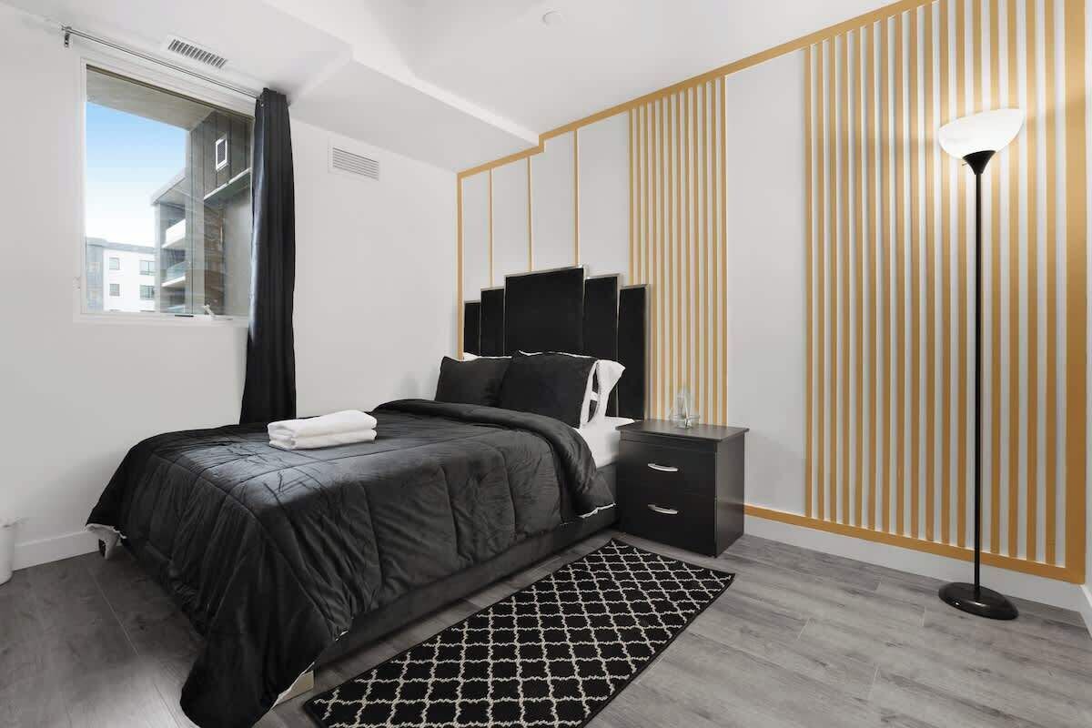 Stylish bedroom with a plush queen bed, coordinating nightstand, floor lamp, geometric rug, large window with blackout curtains, and modern striped accent wall for a restful retreat.