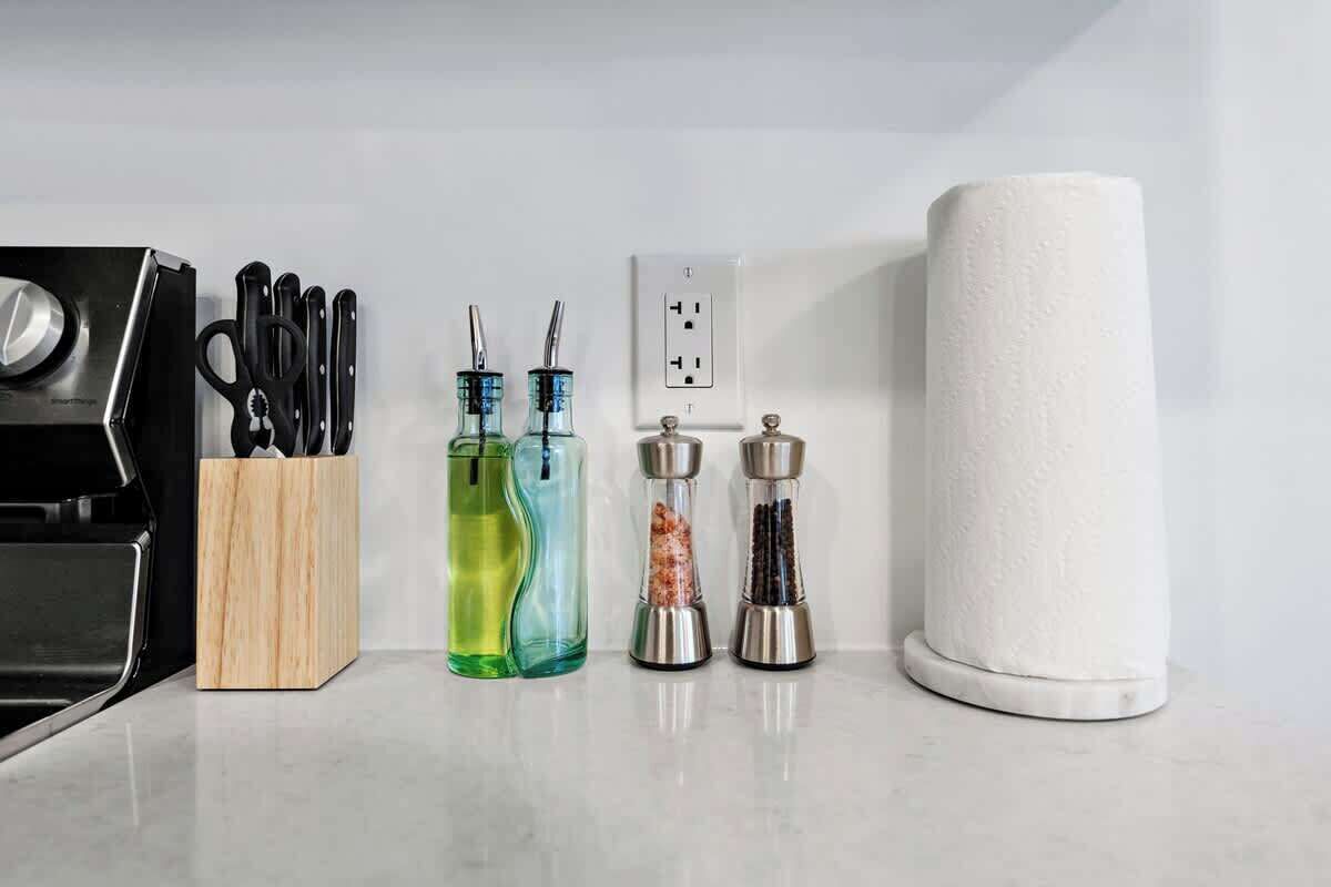 Well-organized countertop featuring sharp knife set, versatile scissors, stylish oil dispensers, elegant salt and pepper grinders, and a handy paper towel roll for convenience.