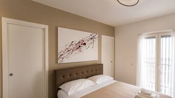 A bedroom with a large bed, a headboard, a painting on the wall, and a window with curtains.