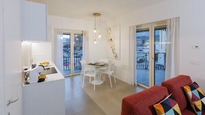 Una sala de estar moderna con un sofá rojo, un comedor con sillas blancas, una cocina con encimera blanca y ventanas amplias con vistas a la ciudad.