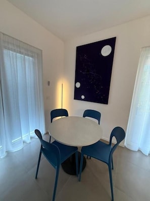 A dining area with a round table, four chairs, and a wall-mounted artwork. - ZENIT APPARTAMENTI & SPA (Terni)