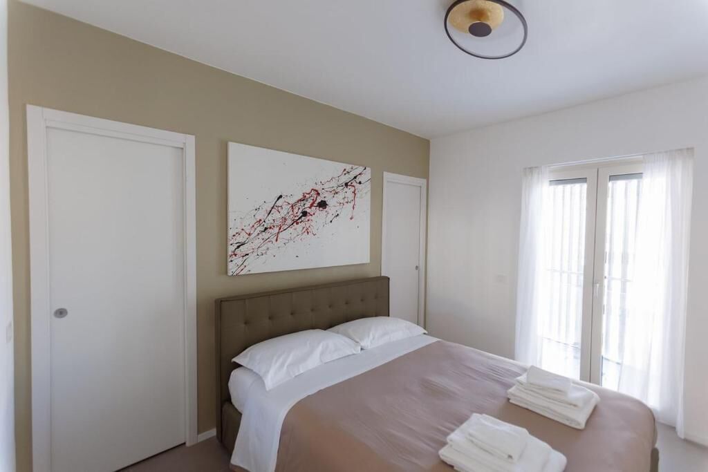 A hotel room with a bed, a large abstract painting, a window with curtains, and a door.