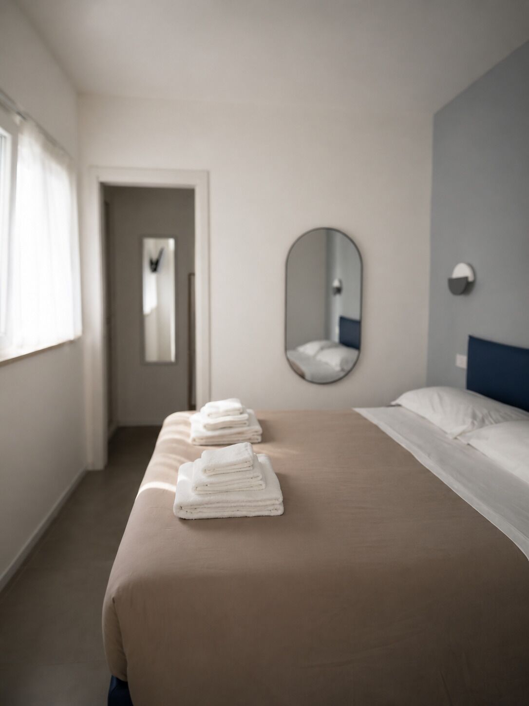 A hotel room with a bed, a mirror, and a stack of towels.