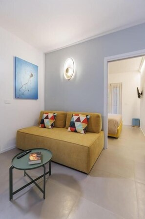 A modern living room with a sofa, a glass coffee table, a painting on the wall, and a door leading to another room. - ZENIT APPARTAMENTI & SPA (Terni)