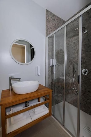 A bathroom with a wooden vanity, a round mirror, a white sink, and a glass-enclosed shower. - ZENIT APPARTAMENTI & SPA (Terni)