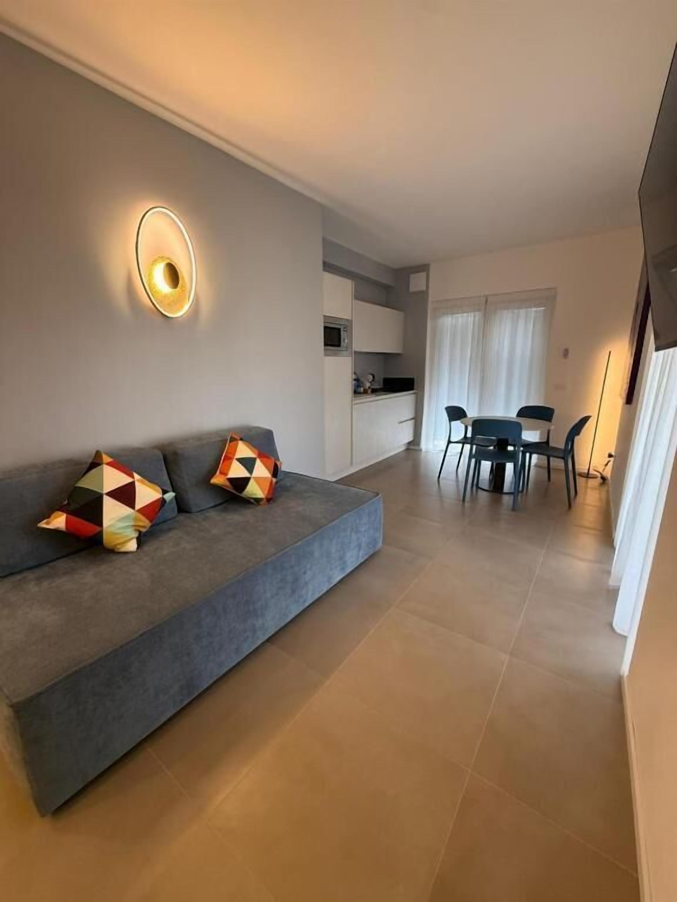 A modern living room with a sofa, a dining table, and a kitchen area in the background.